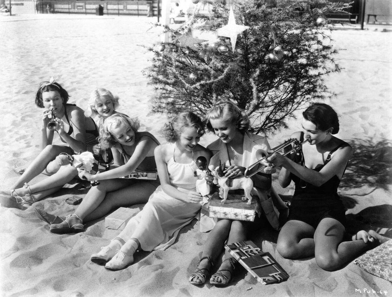 Hollywood Stars Maxine Jennings, Lucille Ball, Phyllis Brooks, Anne Shirley, Jane Hamilton, And Kay Sutton With A Christmas Tree And Presents On Santa Monica Beach, California - December 1935 (Rko Radio Pictures Publicity)