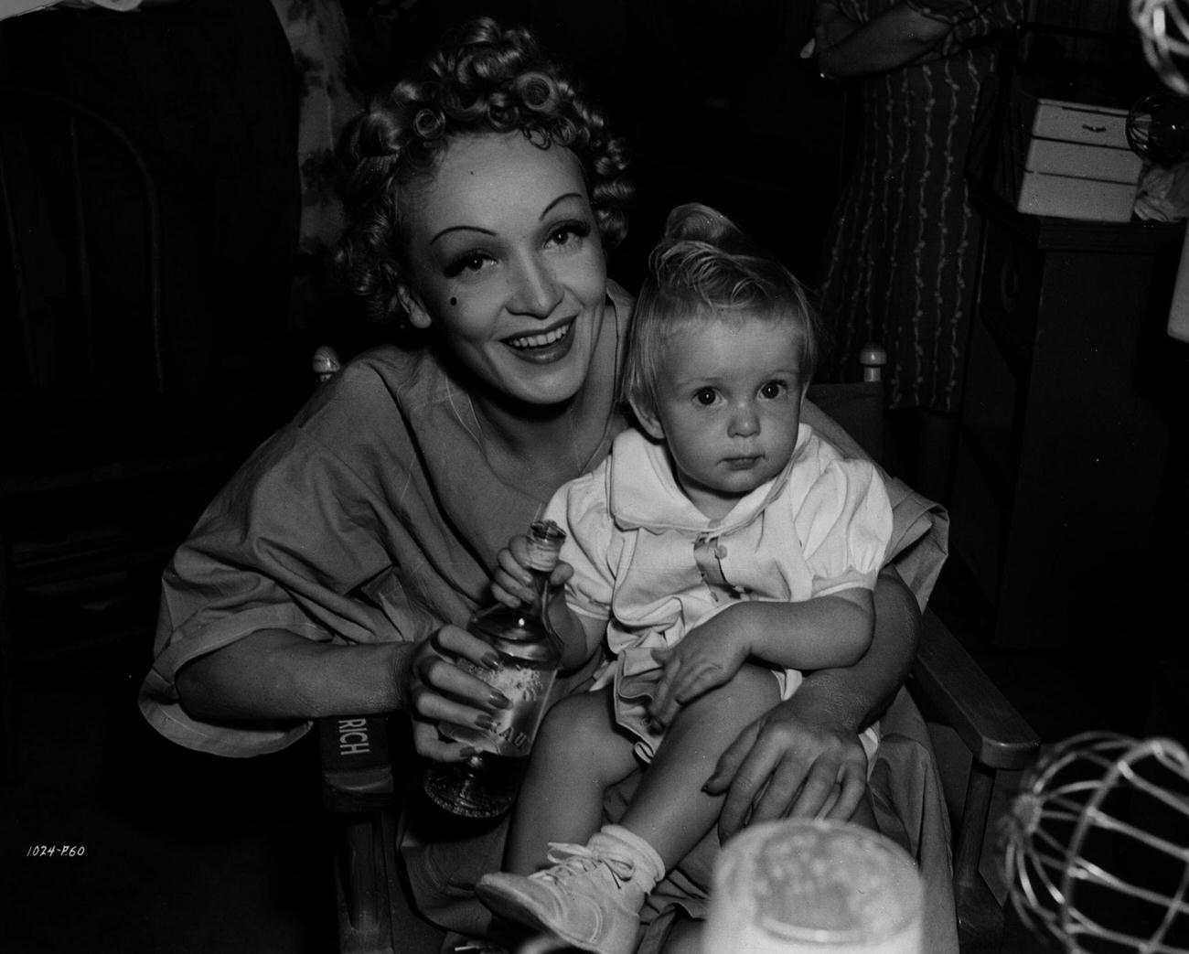 Marlene Dietrich On The Set Of 'Destry Rides Again' Holding Child Actress Baby Sandy (Sandra Lee Henville) During Her Visit From The Set Of Another Universal Picture, 'Little Accident'.