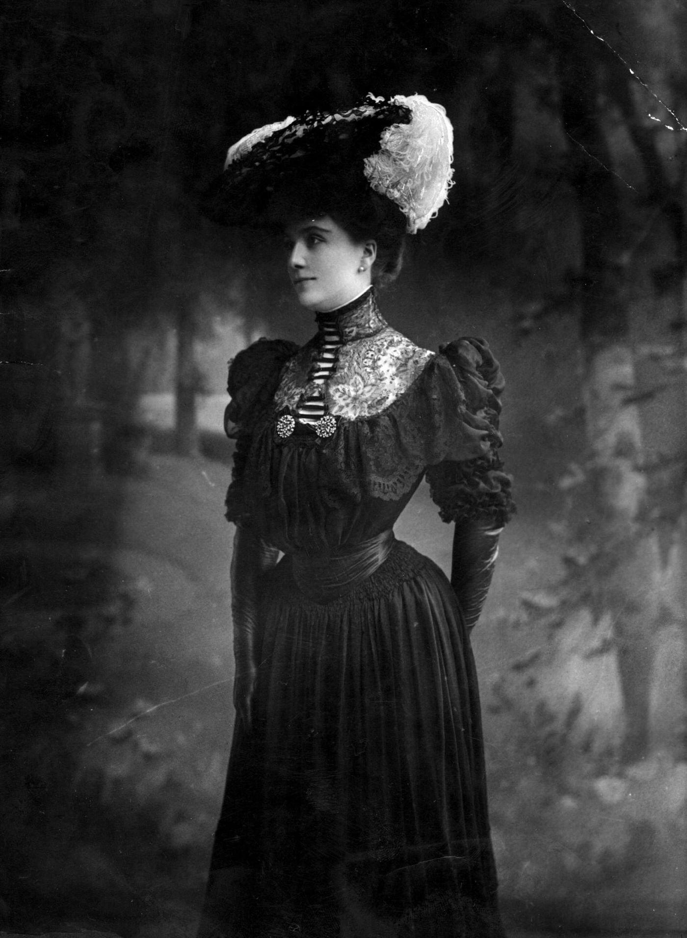 Miss Lewis Wearing A Dark Period Dress With Alluring Lace Detail At The Throat, Set Off Beautifully By A Feather Trimmed Hat.
