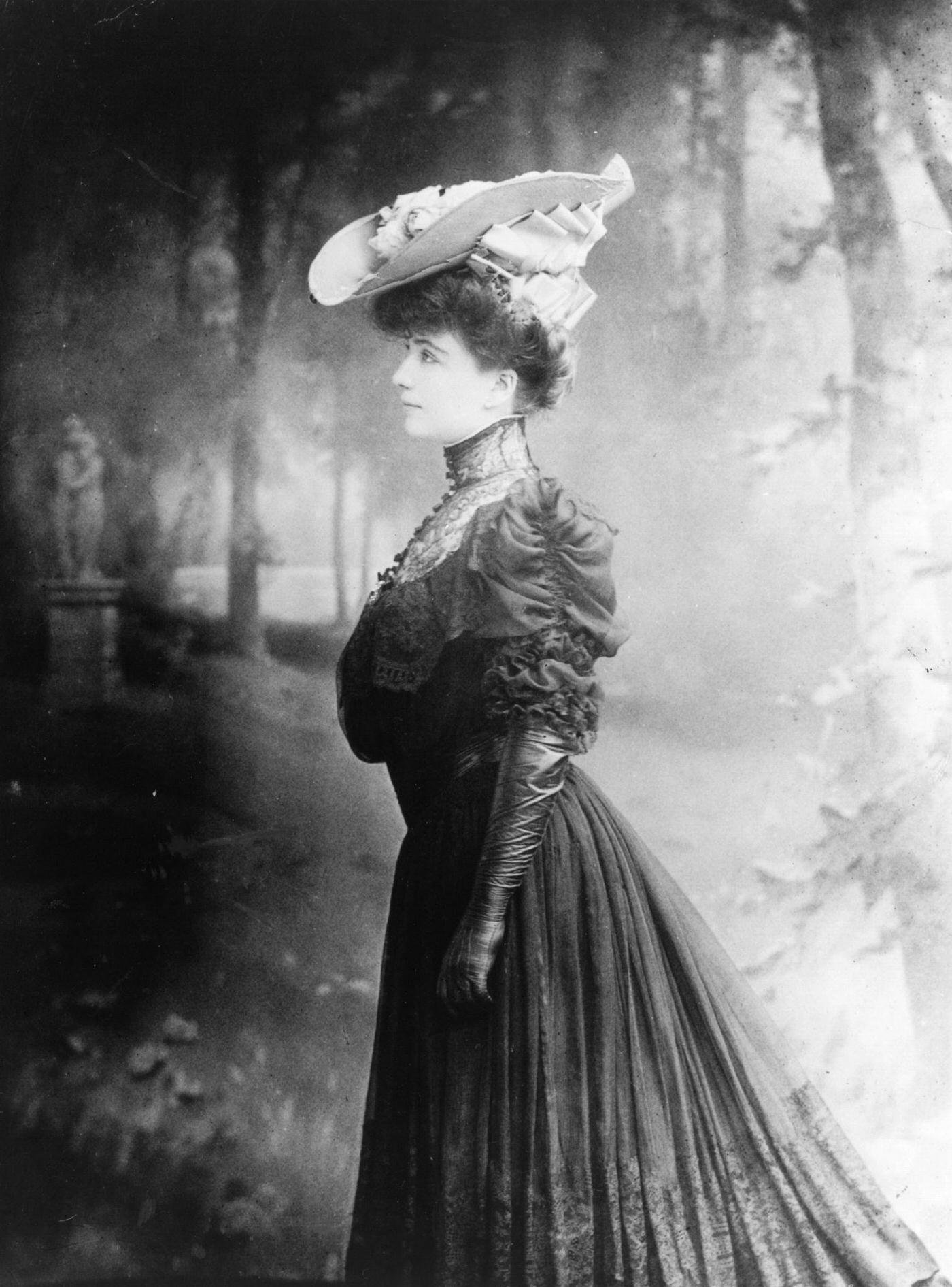 Edwardian Woman Wearing A Fashionable Outfit. A Lustrous Diffusion Of Light Enhances The Ambient Backdrop Of Woodlands Behind Her, 1905