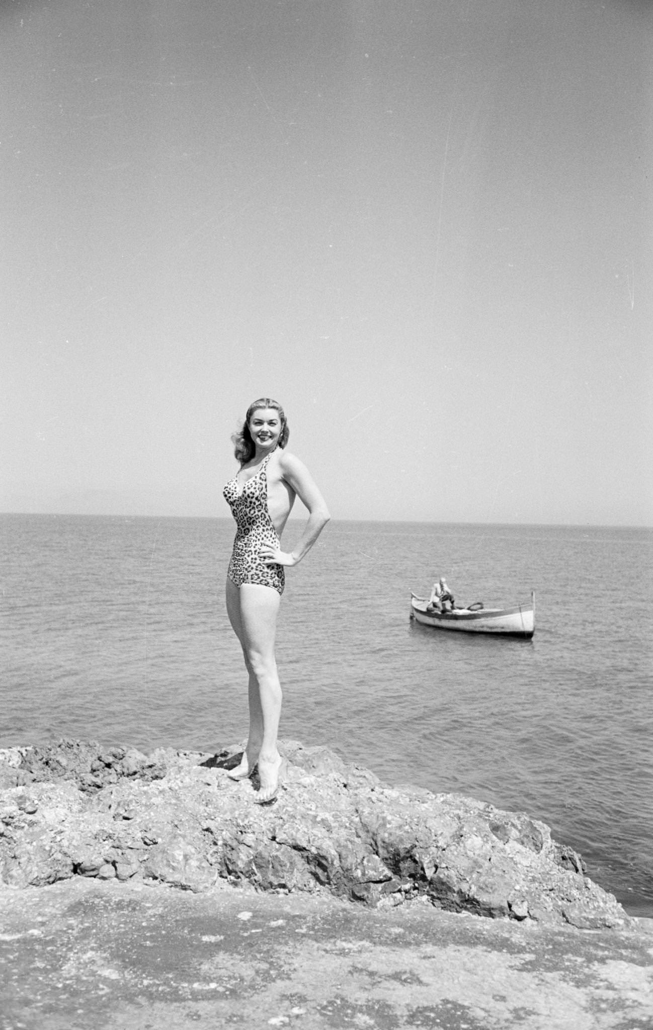 Esther Williams Standing On A Rock In Transparent Pumps, In A Leopard Swimsuit, Hands On Her Hips.