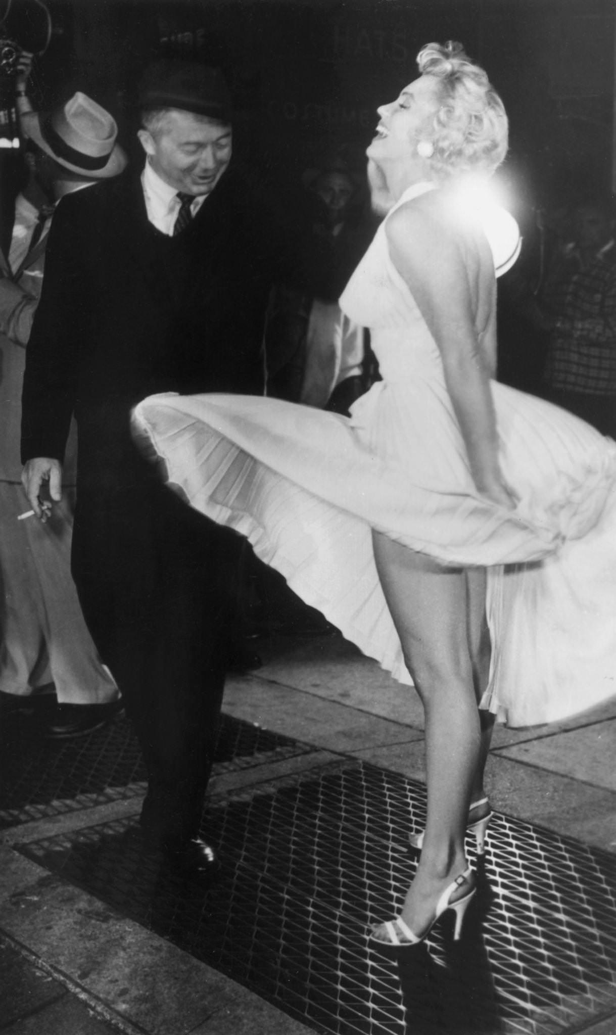 Marilyn Monroe Stands On A Subway Grate And Laughs As The Wind Blows The Skirt Of Her White Halter Dress Next To Austrian-Born Director Billy Wilder