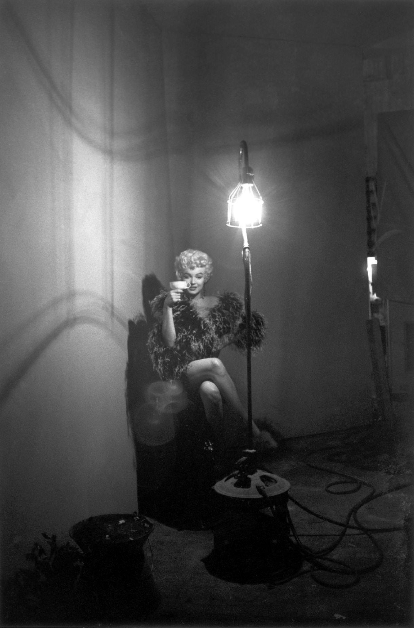 Marilyn Monroe In A Feather Boa Holding A Teacup As She Sits Next To A Tall Floor Lamp In 1954 During The Filming Of &Amp;Quot;The Seven Year Itch&Amp;Quot; In Los Angeles