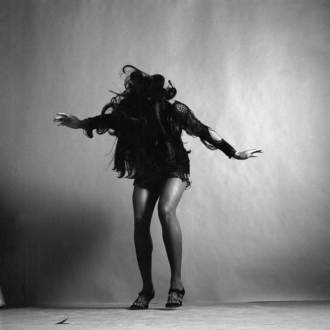 Tina Turner, Wearing A Dark Crocheted Mini-Dress, While Looking Down And Stretching Her Arms Out To The Side, 1969.
