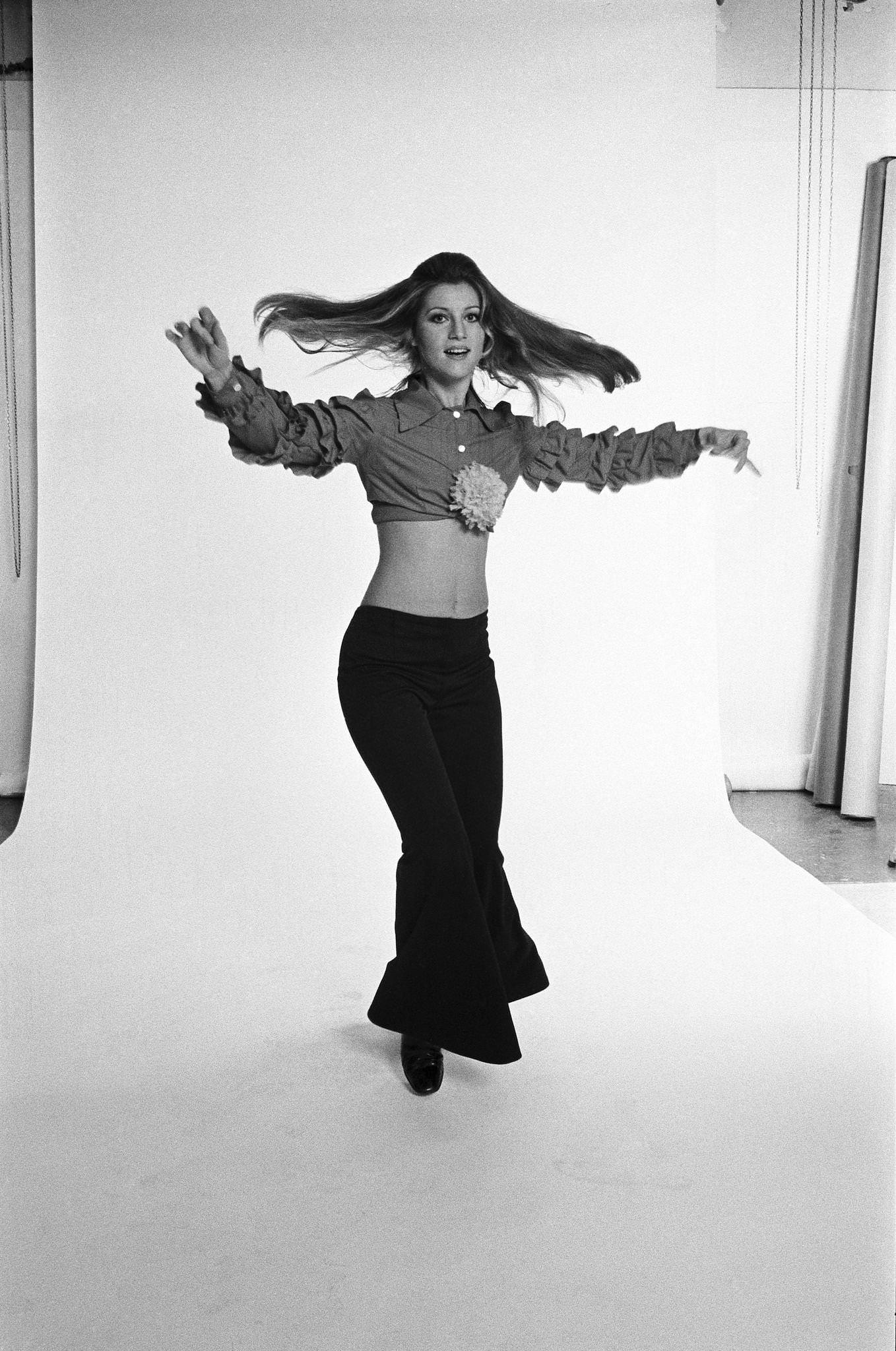 Sheila In Low-Waisted Pants And Ruffled Sleeveless Shirt, Dancing With A Yellow Flower Between Her Breasts