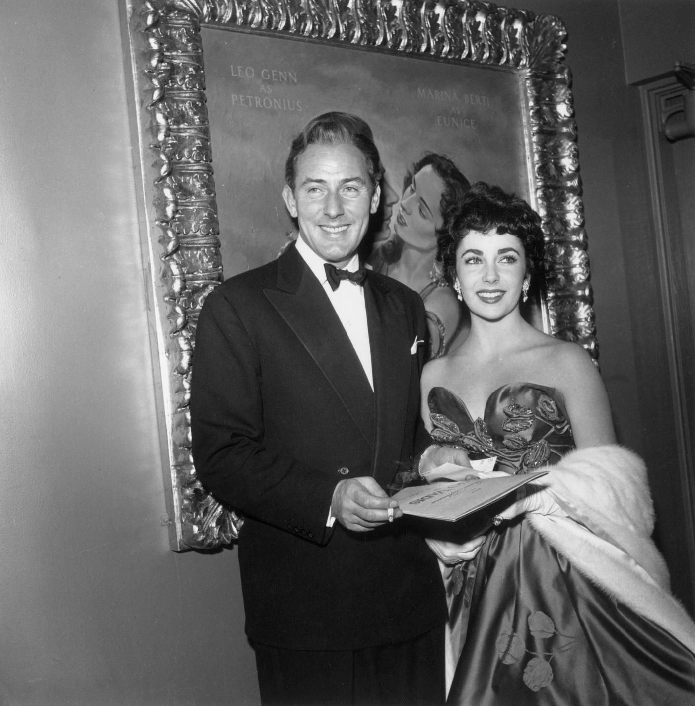 Elizabeth Taylor And Michael Wilding At The Premiere Of Director Mervyn Leroy'S Film, 'Quo Vadis,' Los Angeles, California, 1951. A Gilt-Framed Painting Of Leo Genn As Petronius And Marina Berti As Eunice From 'Quo Vadis' Hangs Behind The Couple. Taylor Played A Cameo Role In The Film.