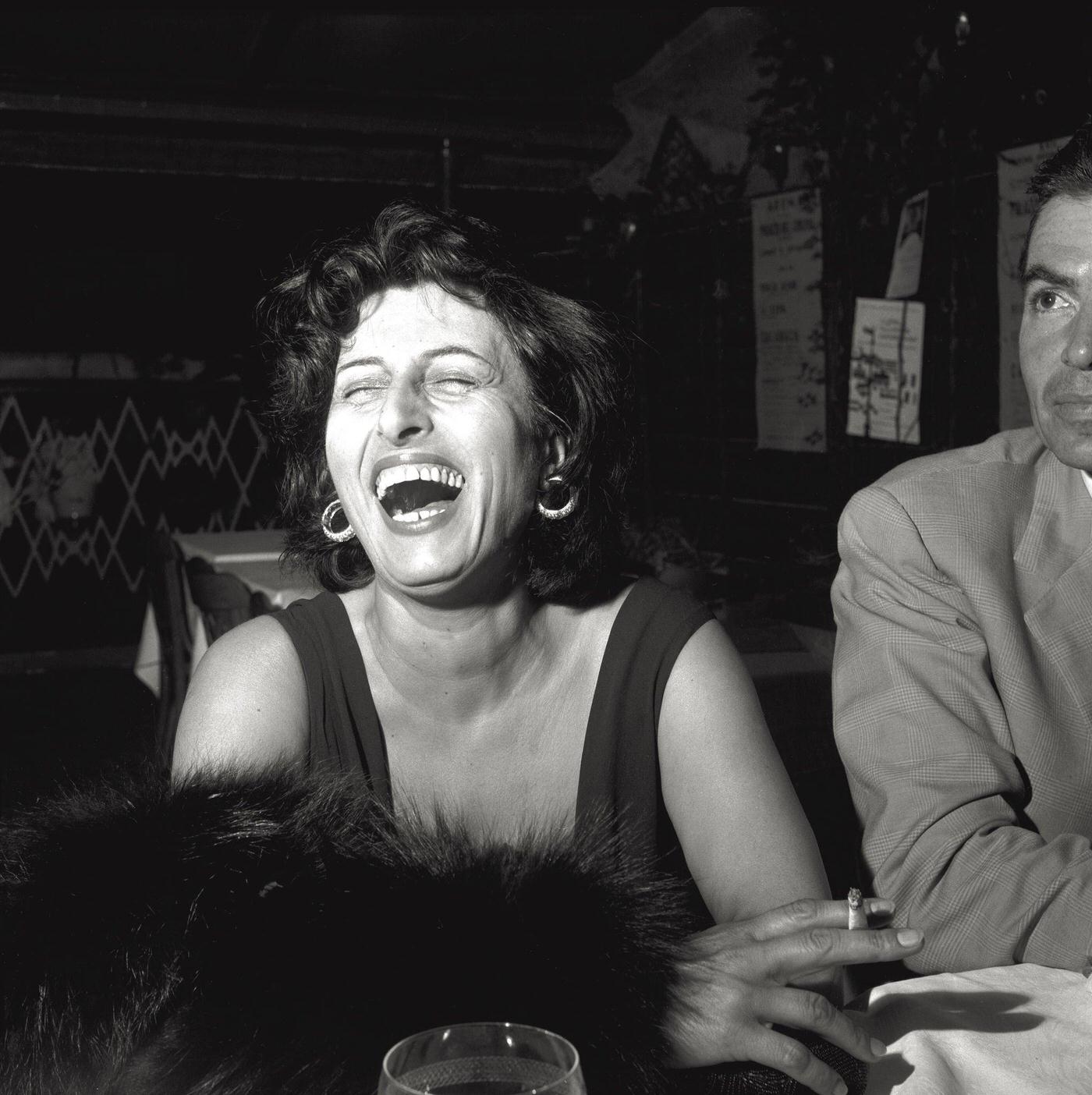 Anna Magnani Laughs Heartily While Sitting At A Table Holding A Fur Coat In Venice, 1956.