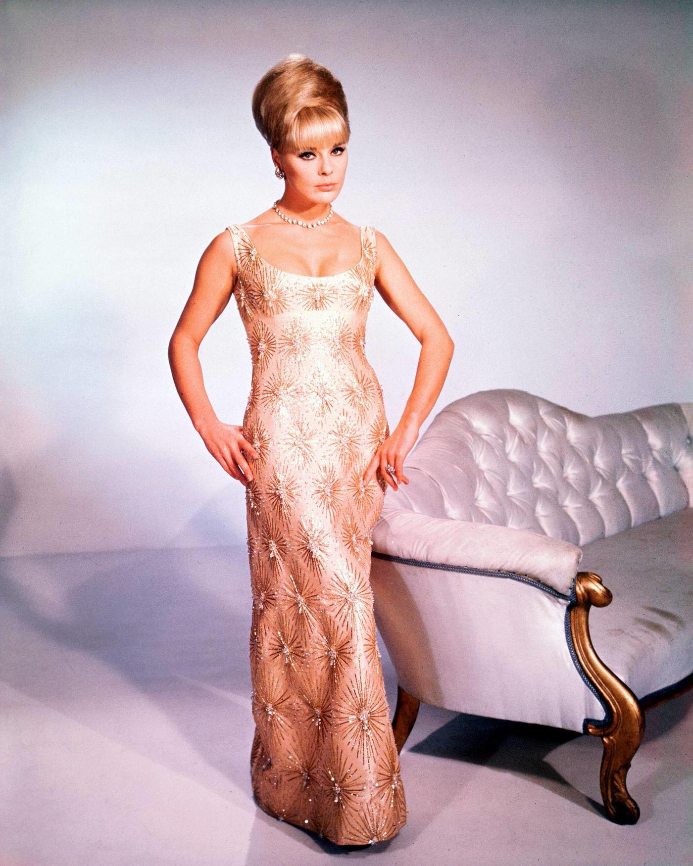 Elke Sommer, Poses In A Long Sleeveless Dress And Beehive Hairstyle, Standing By A Sofa In A Studio Portrait, 1965.
