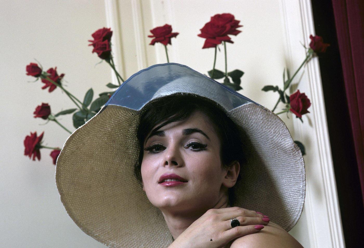 Portrait Of Gila Golan In March 1966, Wearing A Capeline And Standing In Front Of A Bouquet Of Roses.