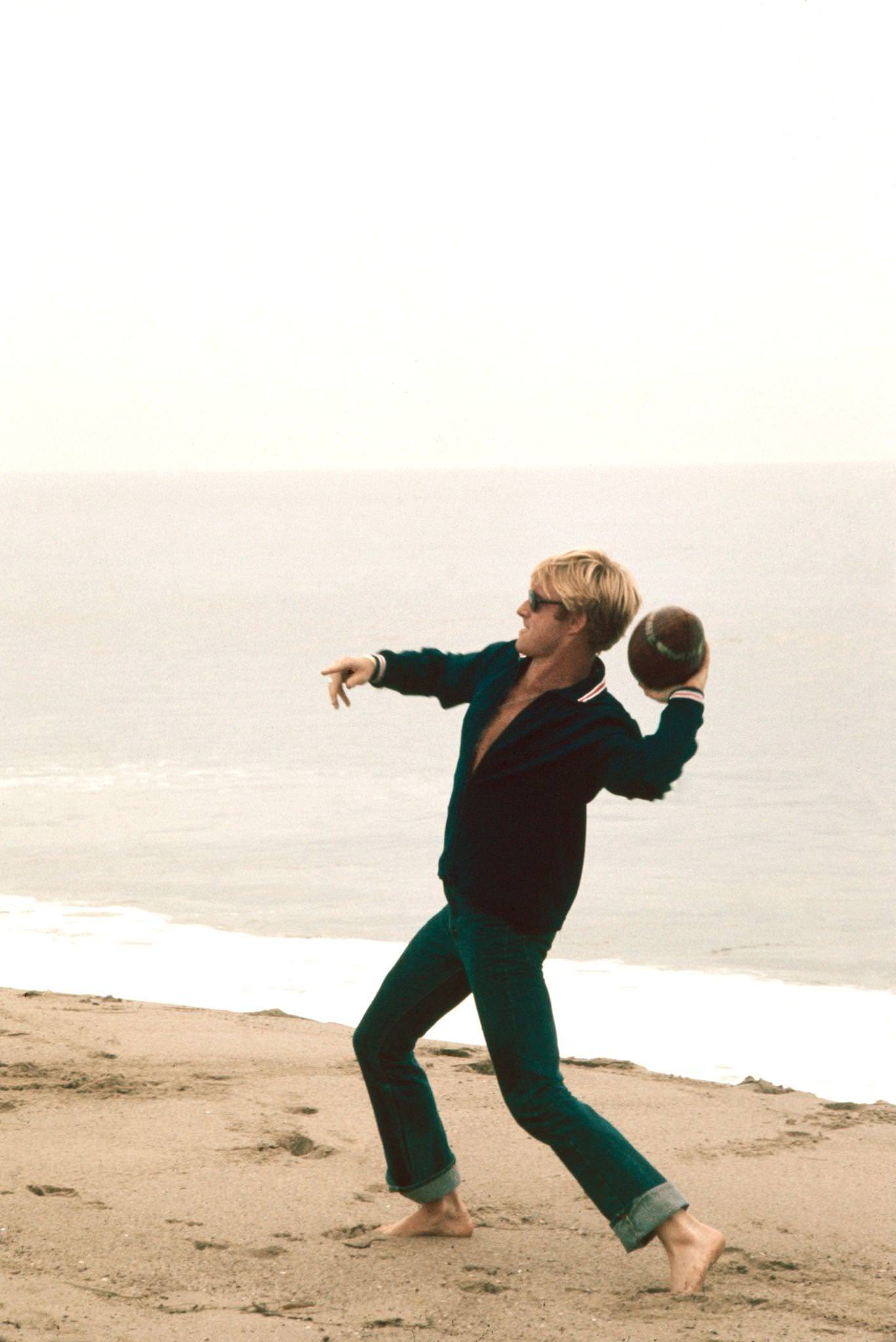 Robert Redford Throwing A Football On The Beach On The Set Of 'The Way We Were' (Directed By Sydney Pollack), 1972.