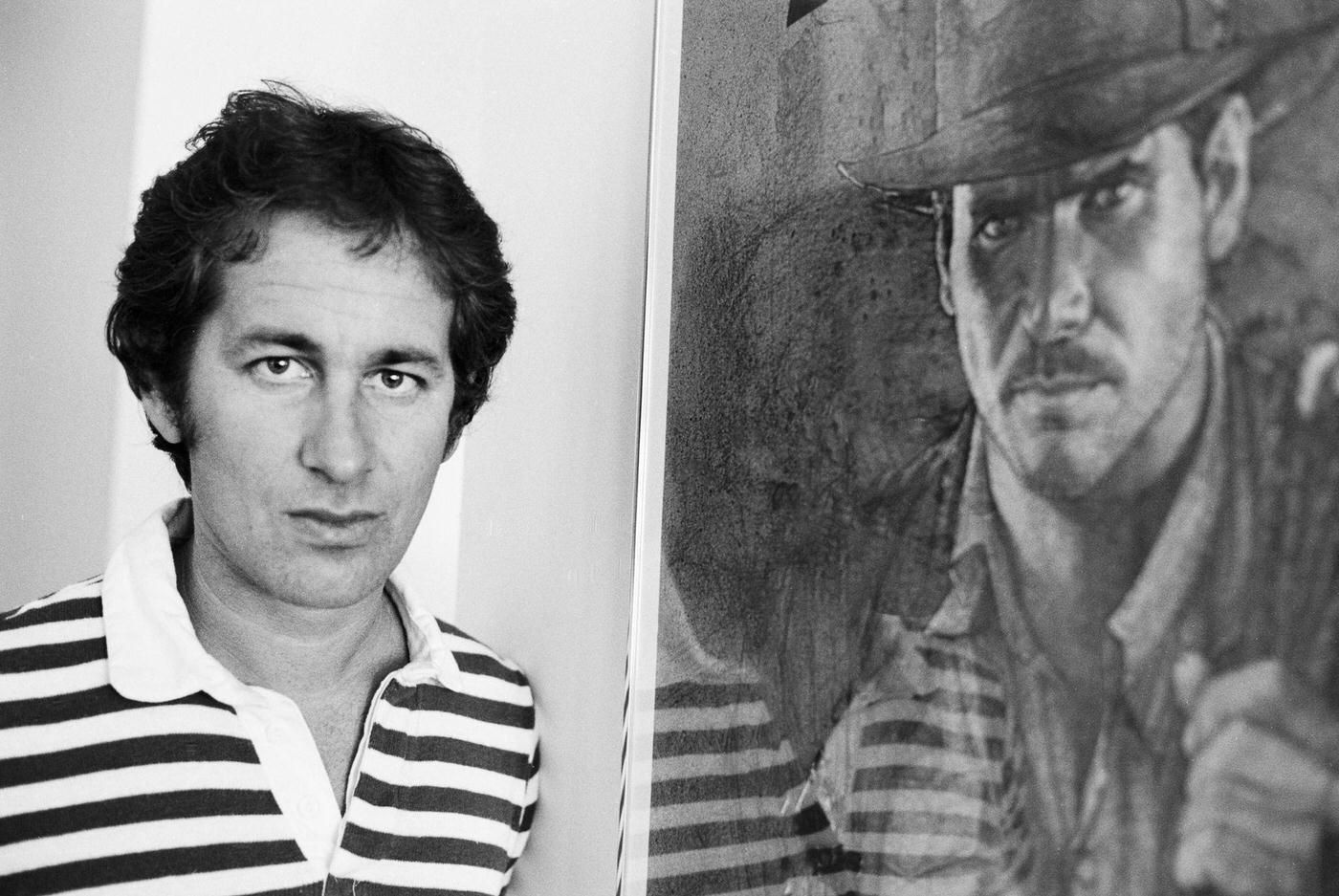 Steven Spielberg Posing Beside A Framed Poster For His Film 'Raiders Of The Lost Ark' In Los Angeles, California, 1981.