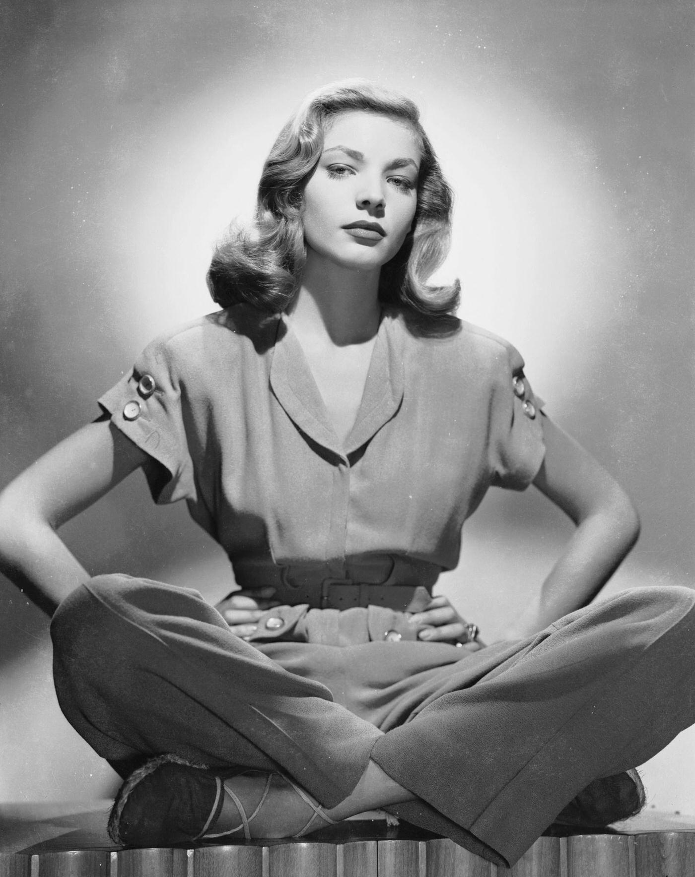 American Screen Star Lauren Bacall Sitting Cross-Legged In A Trouser Suit, With Her Hands On Her Hips, 1945