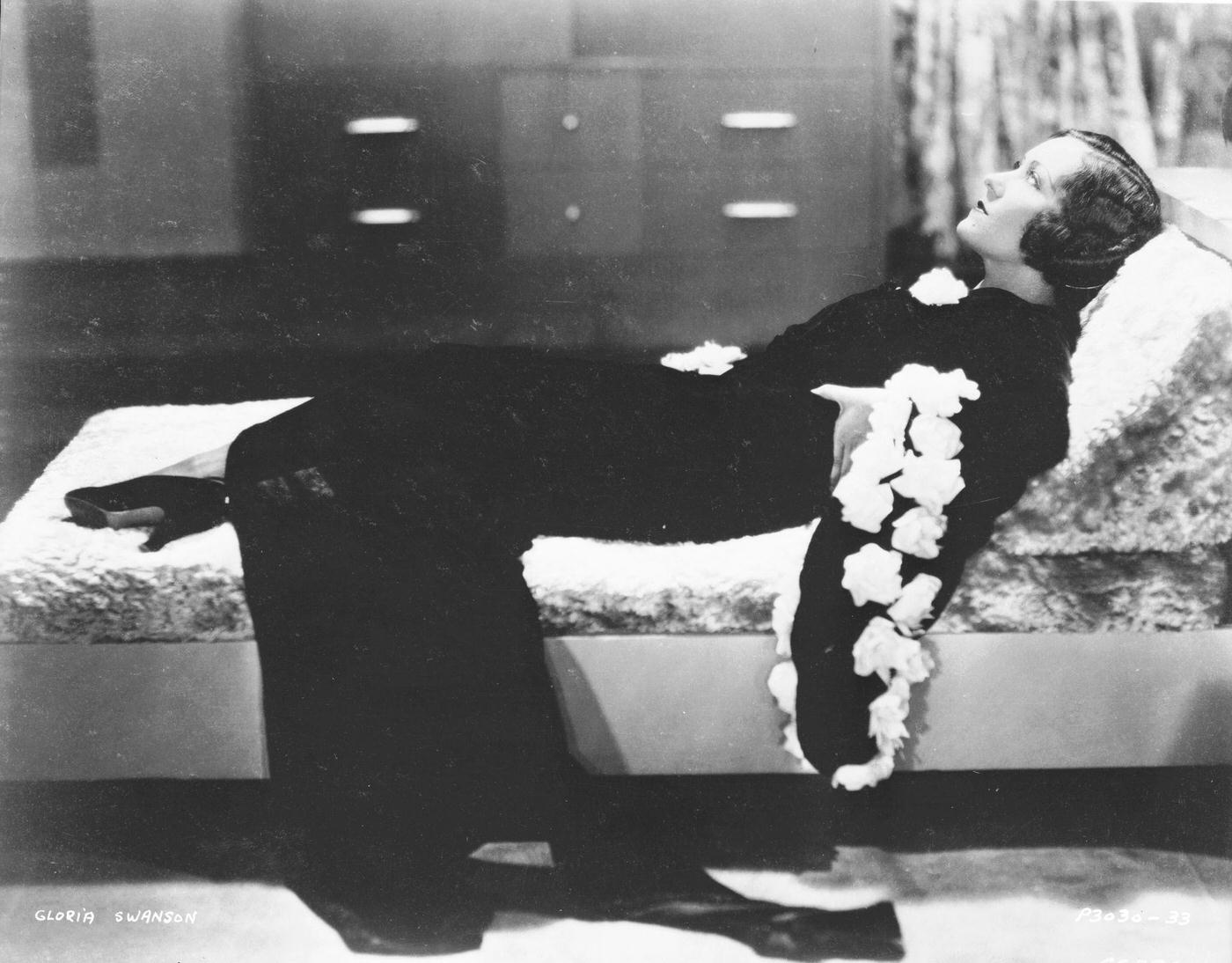 Gloria Swanson Reclines On A Couch In A Dramatic Wide-Sleeved Gown, Circa 1931.