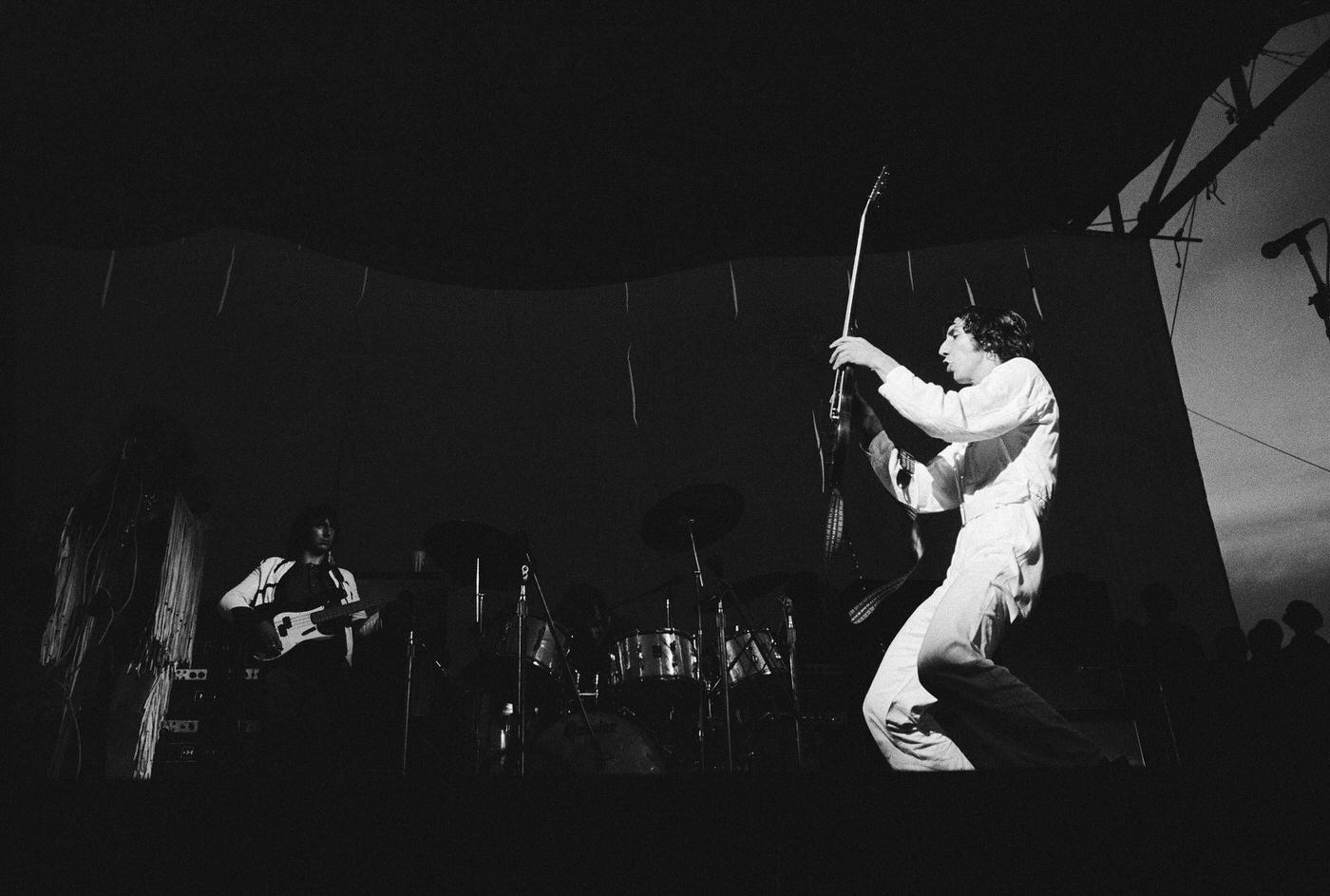 Pete Townshend Holds His Guitar As Roger Daltrey Stands In Shadows During A Concert, Year Unknown.