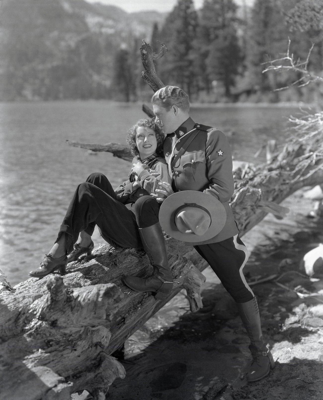 Nelson Eddy And Jeanette Macdonald Embrace, Seated On A Fallen Tree In The Canadian Wilderness In 'Rose Marie,' 1936.