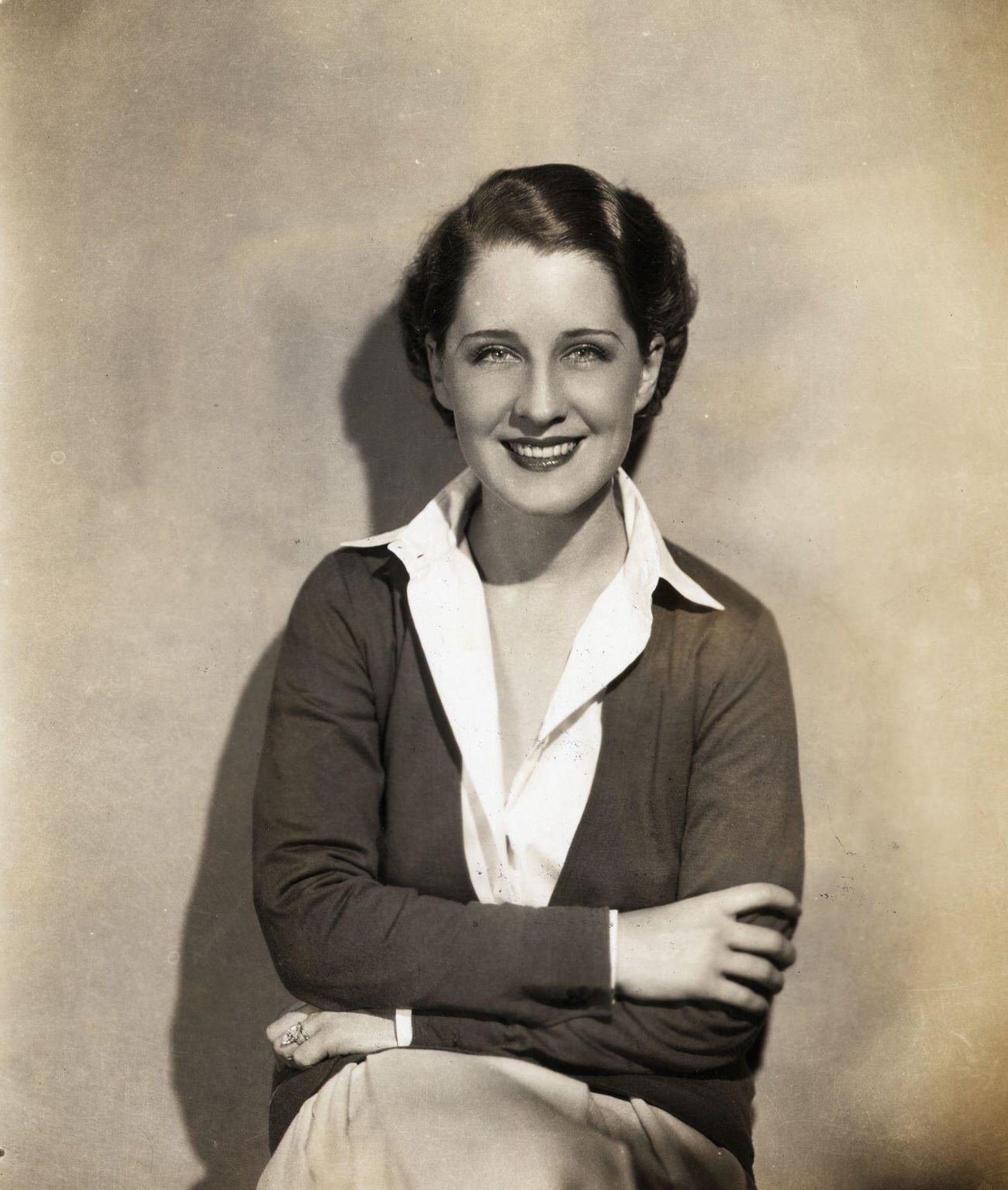 Norma Shearer In A Seated Portrait With Open-Necked Blouse, Arms Folded Across Her Chest.
