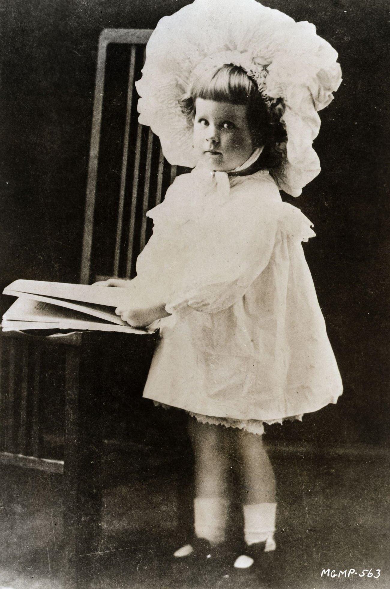 Young Norma Shearer In A Large Baby Bonnet And A Short White Period Dress, Posed As If Reading A Book.