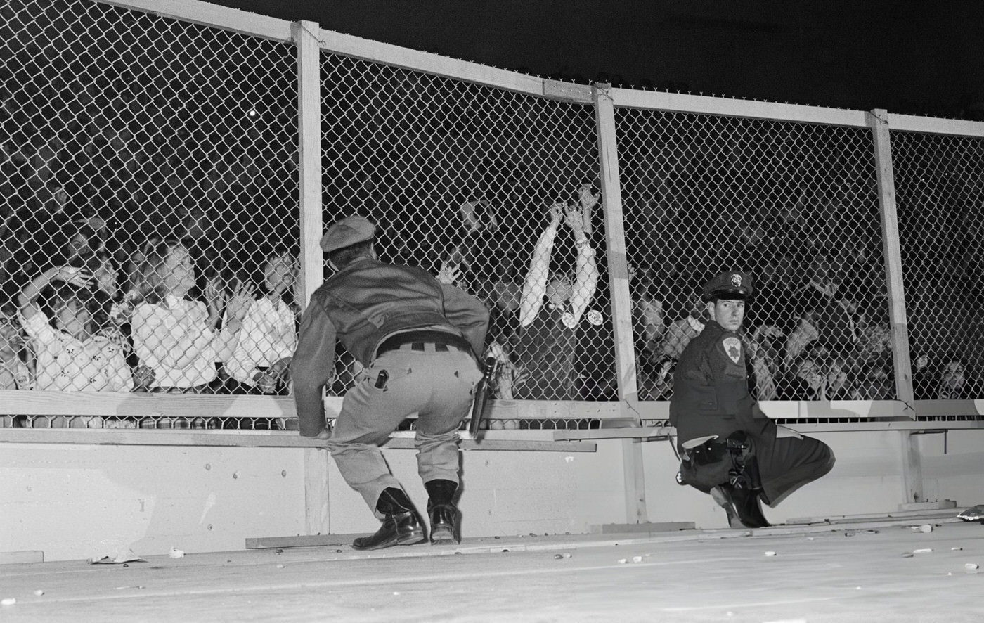 Police Officers And A Wire Fence Keep Fans At Bay During A Beatles Concert At The Cow Palace In Daly City, Near San Francisco, California, During Their Summer 1964 United States And Canada Tour.