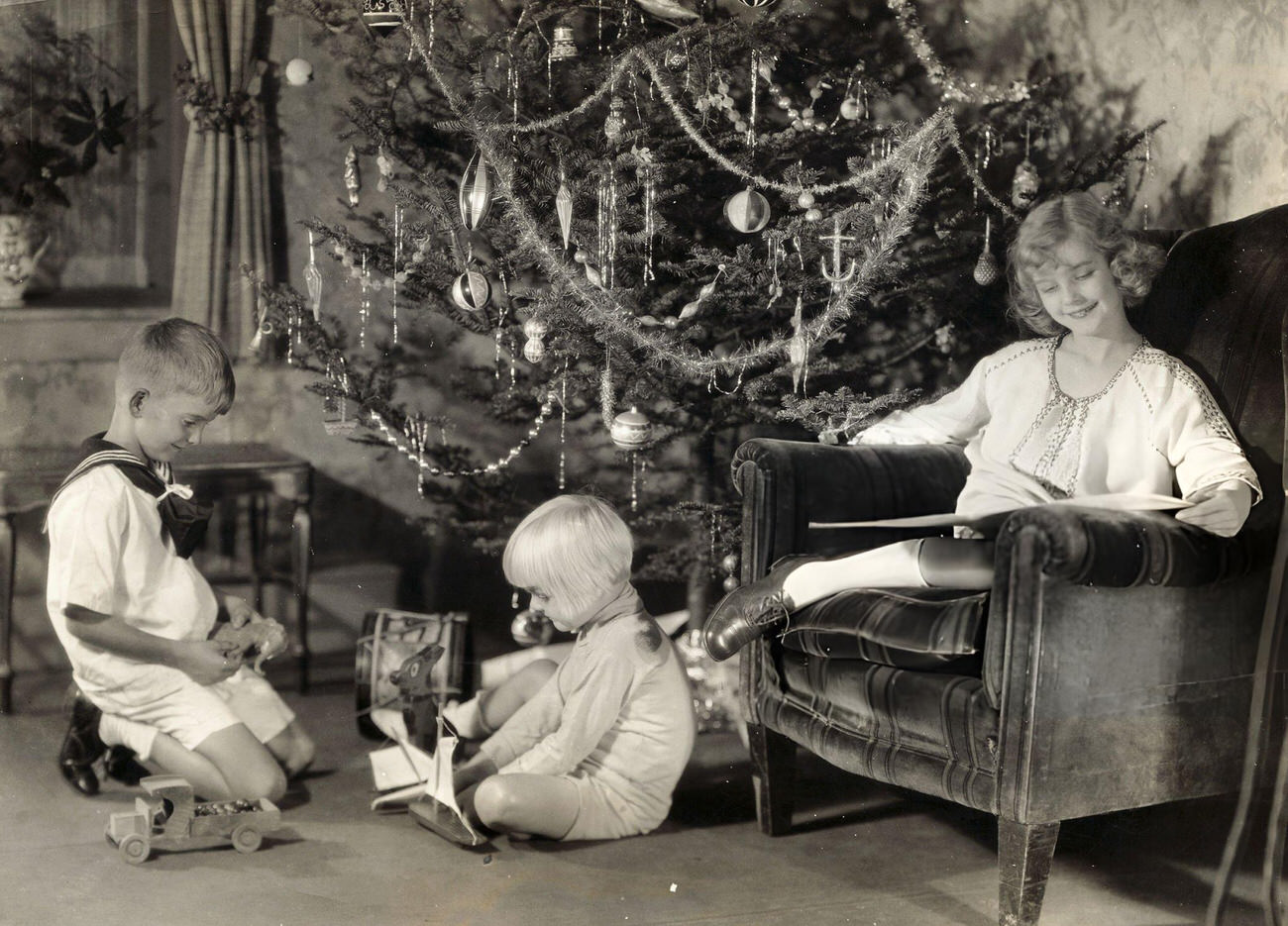 Anita Louise Reading A Book While Two Other Children Play With Their Presents Under A Christmas Tree, Circa 1927.