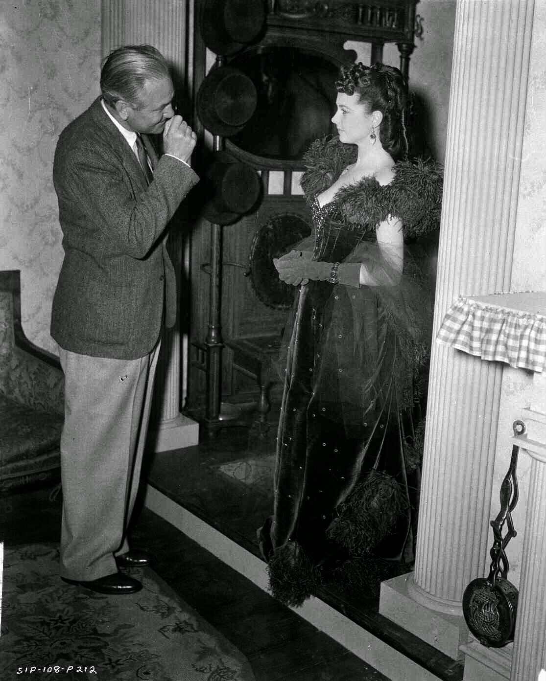Victor Fleming Looking At Vivien Leigh As Scarlett O'Hara, Who Is Standing In Doorway, Wearing Red Gown.