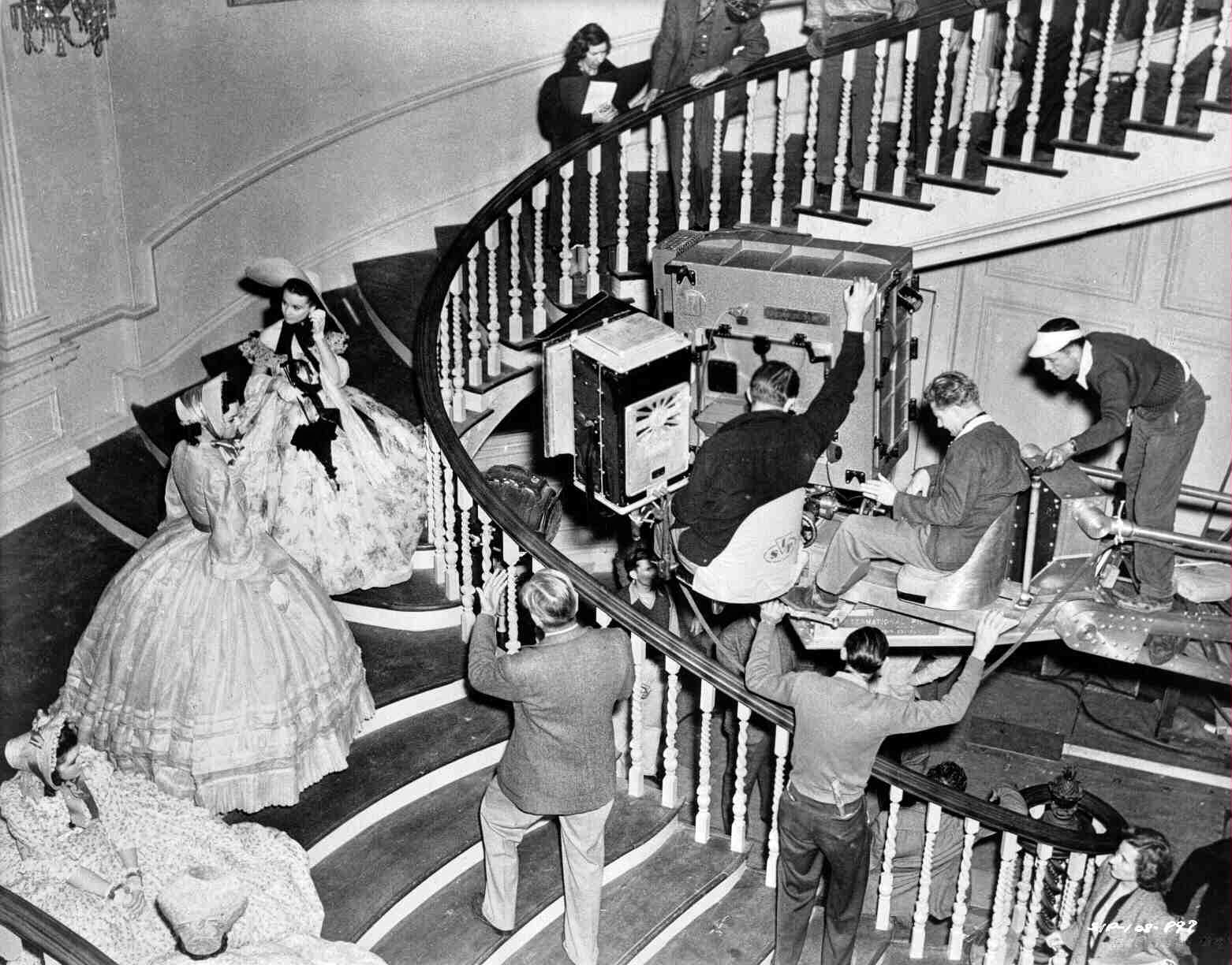 Marcella Martin As Cathleen Calvert On Staircase At Twelve Oaks, Talking To Vivien Leigh As Scarlett O'Hara. Director Victor Fleming Stands On Stairs Back To Camera. Technicians, Crew, And Extras Surround.