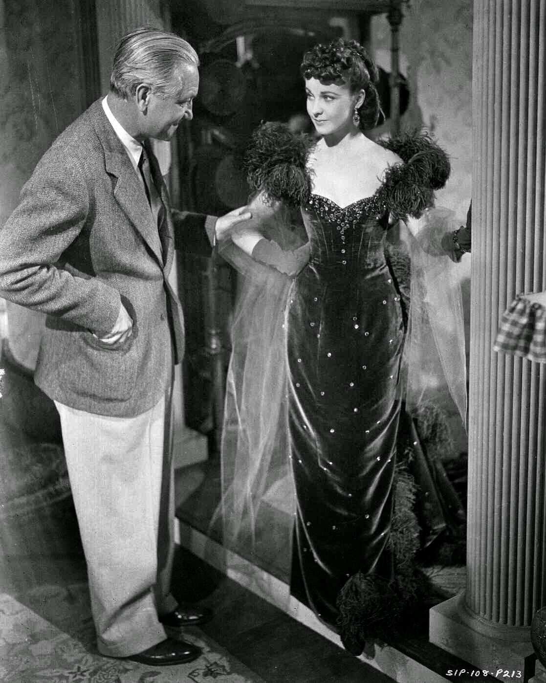 Director Victor Fleming Looking At Vivien Leigh As Scarlett O'Hara, Who Is Standing In Doorway, Wearing Red Gown.