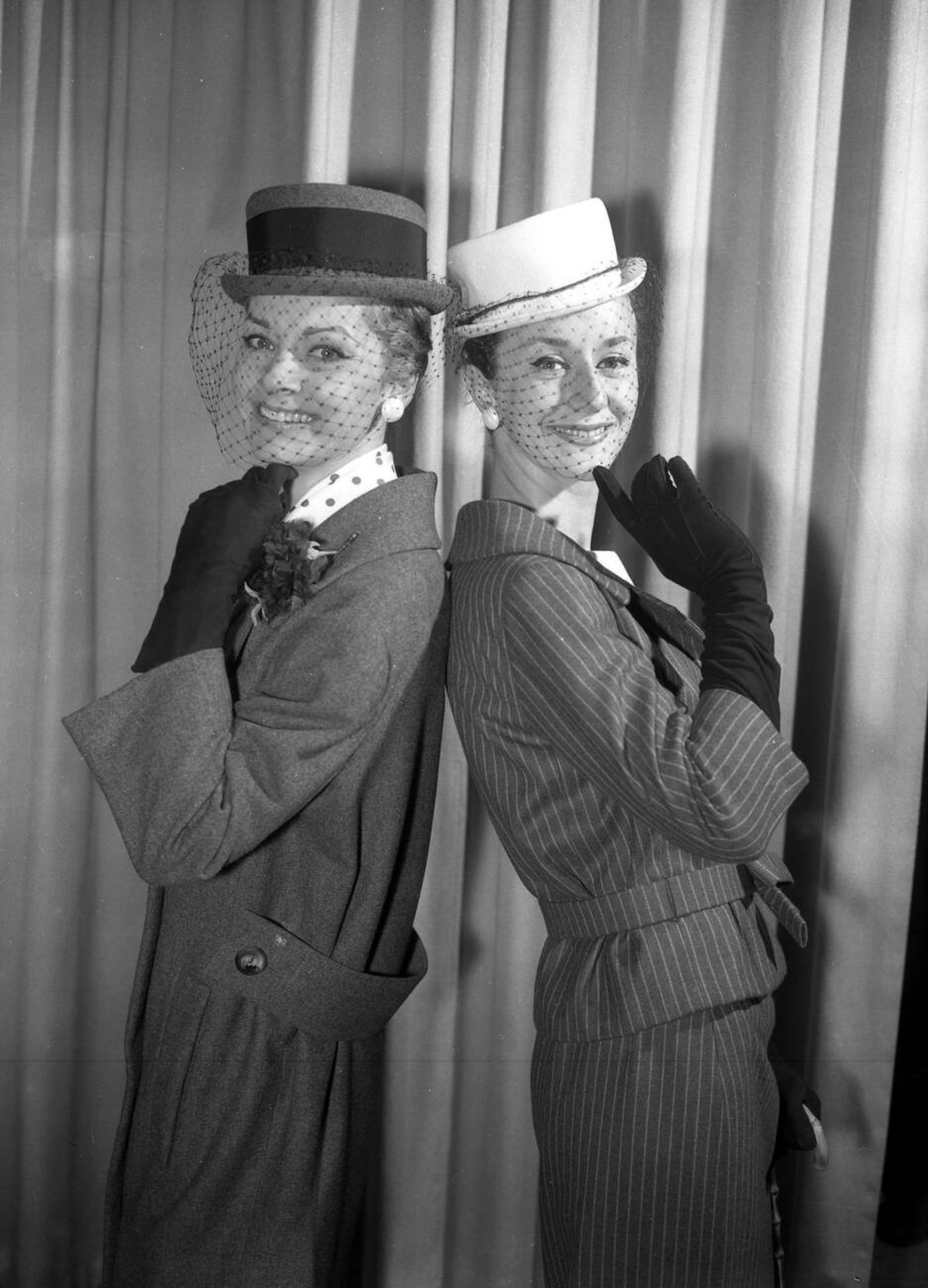 Two Outdoor Styles, A Grey Flannel Raspet Coat With Belted Back And A Wool Suit In Grey With White Pinstripe, Are Pictured During A Showing Of The Christian Dior - London Fashion Collection For Summer, 1959.