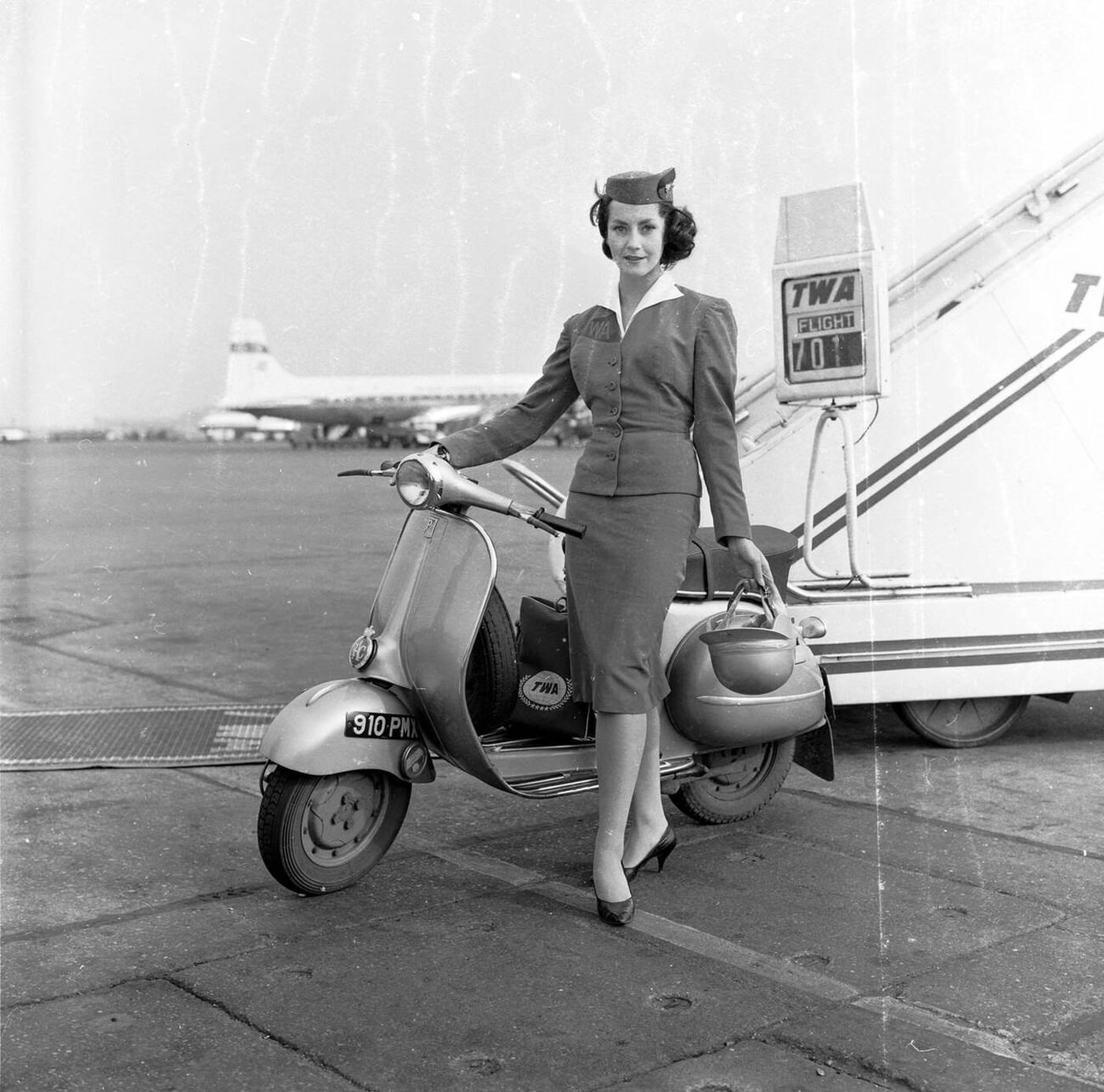 A Glamorous Twa Air Stewardess Stands With Helmet By Her New Mode Of Transport At The Boarding Steps Of A Plane, London Aiport, 1960.