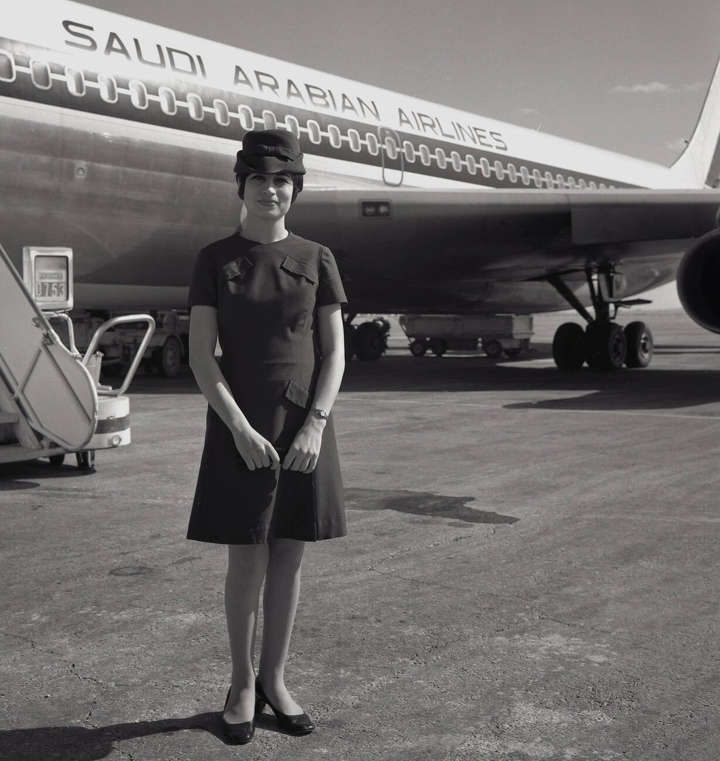 Uniformed Female Air Hostess Standing Outside A Saudi Arabian Airlines Jet Aircraft, Heathrow Airport, 1960.