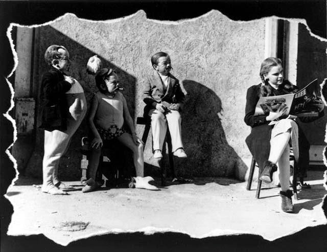 Judy Garland Reads A Copy Of Life Magazine On Set As Three Of The Actors Playing Munchkins Stand By.