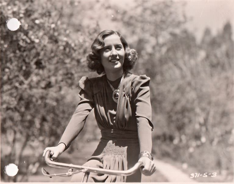 Barbara Stanwyck Riding A Bicycle Down A Country Lane.