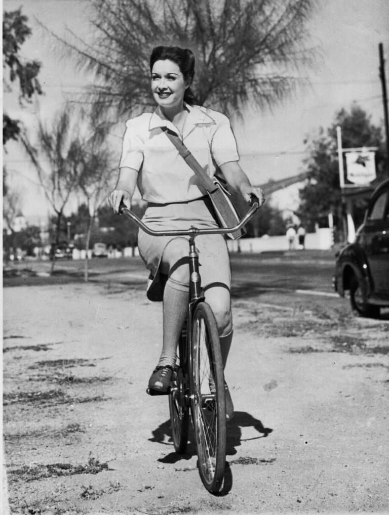 Gail Patrick Riding A Bicycle Past A Gas Station In Hollywood, 1942.